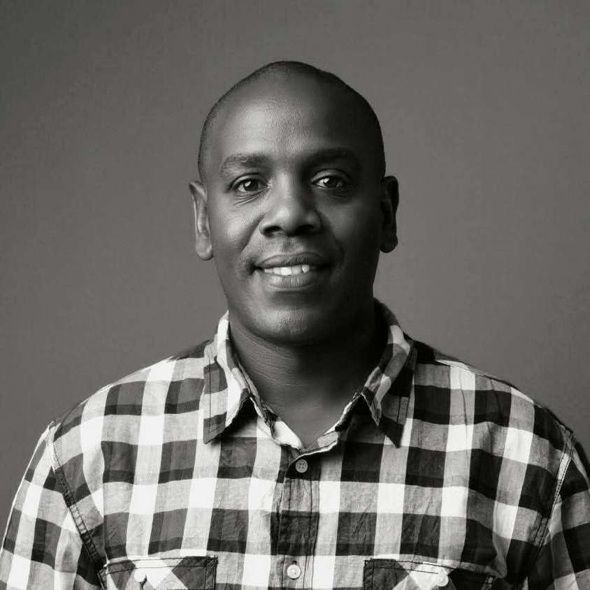 Black and white studio portrait of Enock Change in a checked shirt