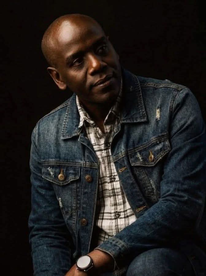 Portrait of Enock Change in a denim jacket against a dark background
