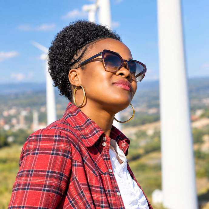 Grace Mafuta wearing sunglasses and a red plaid shirt with wind turbines behind