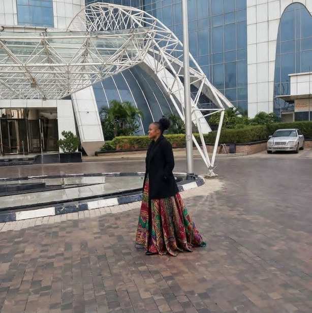 Aidah Balukah standing in an African print skirt outside a glass building